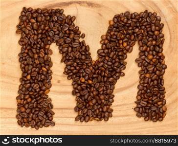 Letter M, alphabet from coffee beans. isolated on wood