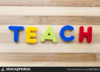 "Letter magnets "TEACH" closeup on wood background "