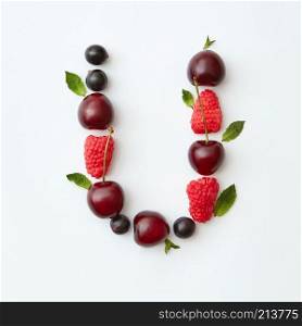 Letter U english alphabet in the form of a pattern of natural organic berries - ripe fresh raspberry, black currant, cherry, green mint leaf isolated on a white background. Top view.. Fresh berries pattern of letter U english alphabet from natural ripe berries - black currant, cherries, raspberry, mint leaf isolated on a white background. Top view.