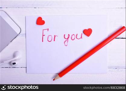 Letter with an inscription in red pencil for you, next to a mobile phone, a white wooden surface