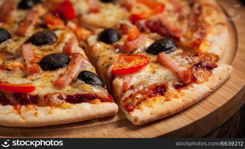 Letterbox panorama of sliced ham pizza with capsicum and olives on wooden board on table. Ham pizza close up letterbox