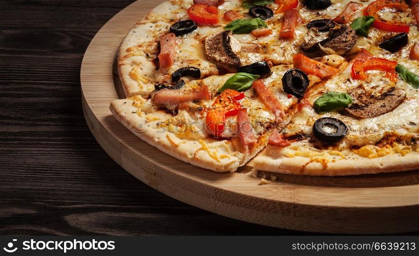 Letterbox panorama of sliced ham pizza with capsicum and olives on wooden board on table. Ham pizza close up letterbox