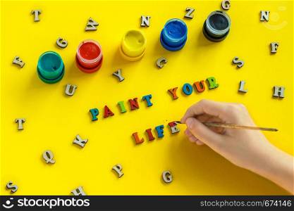 Lettering Paint your life from colorful letters, hand with paintbrush, gouache, scattered wooden letters. yellow background, greeting card. Concept - Paint your life. It's up to you