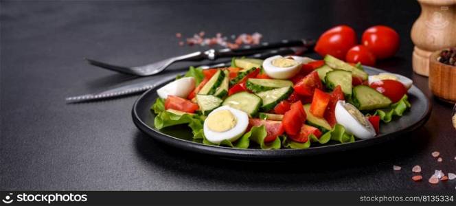 Lettuce, cucumber, spinach, tomato and quail eggs salad with herbs and lemon on black plate on a dark concrete background. Lettuce, cucumber, spinach, tomato and quail eggs salad with herbs and lemon