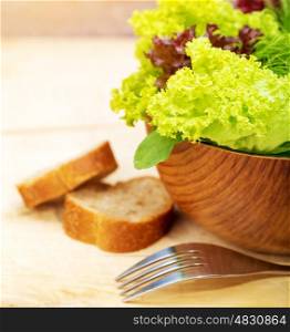 Lettuce salad with two slice of bread on wooden table, shiny fork, fresh green vegetables, organic food, healthy nutrition, dieting concept