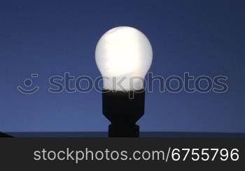 leuchtende Energiesparlampe vor blauem Hintergrund