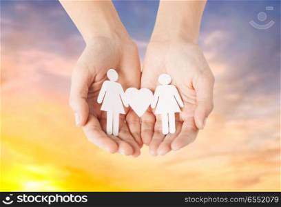lgbt and gay concept - hands holding paper female couple pictogram with heart over evening sky background. female hands holding paper gay couple pictogram. female hands holding paper gay couple pictogram