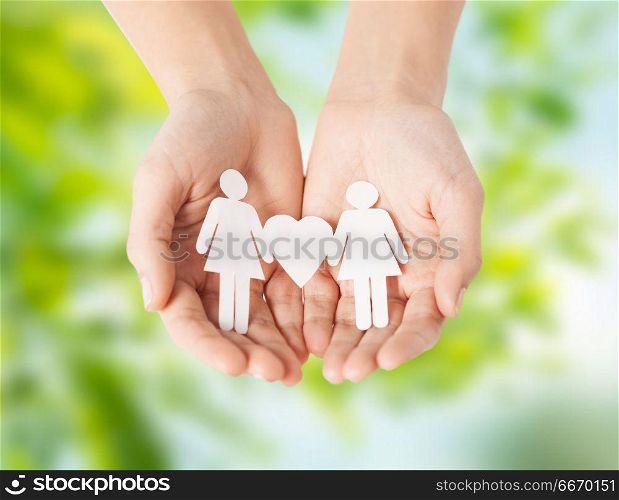 lgbt and gay concept - hands holding paper female couple pictogram with heart over green natural background. female hands holding paper gay couple pictogram. female hands holding paper gay couple pictogram