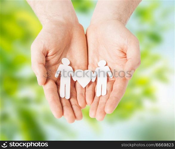 lgbt and gay concept - hands holding paper male couple pictogram with heart over green natural background. male hands holding paper gay couple pictogram. male hands holding paper gay couple pictogram