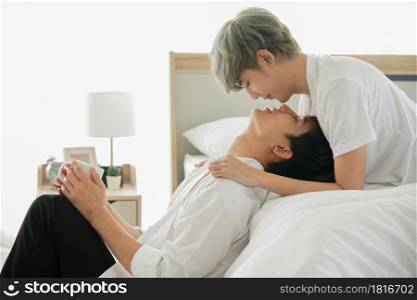 LGBT Asian handsome young gay couple kissing lying on the bed and holding cup of coffee in the morning