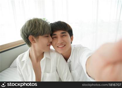 LGBT Asian young gay couple kissing while taking a romantic selfie photo together at bedroom