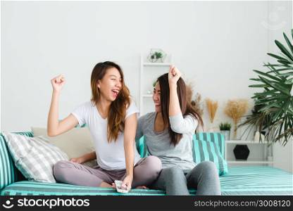 LGBT lesbian women couple moments happiness. Lesbian women couple together indoors concept. Friends young smiling women at home sitting on the couch and watching tv, She is holding a remote control.