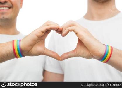 lgbt, same-sex love and homosexual relationships concept - close up of happy smiling male couple wearing gay pride rainbow awareness wristbands showing hand heart gesture. gay couple with rainbow wristbands and hand heart. gay couple with rainbow wristbands and hand heart