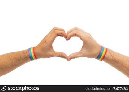 lgbt, same-sex love and homosexual relationships concept - close up of male couple hands with gay pride rainbow awareness wristbands showing heart gesture. male hands with gay pride wristbands showing heart. male hands with gay pride wristbands showing heart