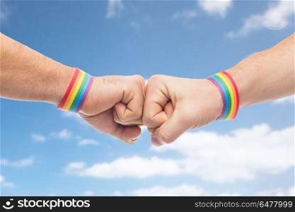 lgbt, same-sex love and homosexual relationships concept - close up of male couple hands with gay pride rainbow awareness wristbands making fist bump gesture over blue sky and clouds background. hands with gay pride wristbands make fist bump. hands with gay pride wristbands make fist bump