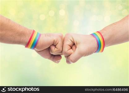 lgbt, same-sex love and homosexual relationships concept - close up of male couple hands with gay pride rainbow awareness wristbands making fist bump gesture over green lights background. hands with gay pride wristbands make fist bump. hands with gay pride wristbands make fist bump