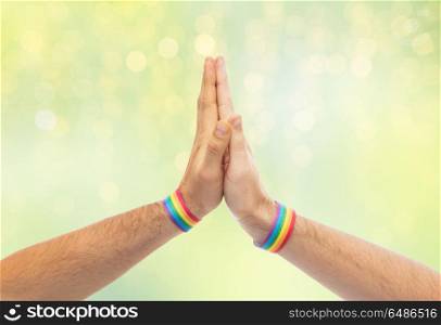 lgbt, same-sex love and homosexual relationships concept - close up of male couple hands with gay pride rainbow awareness wristbands making high five gesture over green lights background. hands with gay pride wristbands make high five. hands with gay pride wristbands make high five