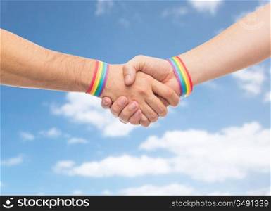 lgbt, same-sex love and homosexual relationships concept - close up of male couple hands with gay pride rainbow awareness wristbands making handshake over blue sky and clouds background. hands with gay pride wristbands make handshake. hands with gay pride wristbands make handshake