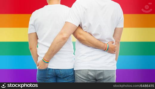 lgbt, same-sex relationships and homosexual concept - close up of hugging male couple wearing gay pride awareness wristbands over rainbow background. male couple with gay pride rainbow wristbands. male couple with gay pride rainbow wristbands