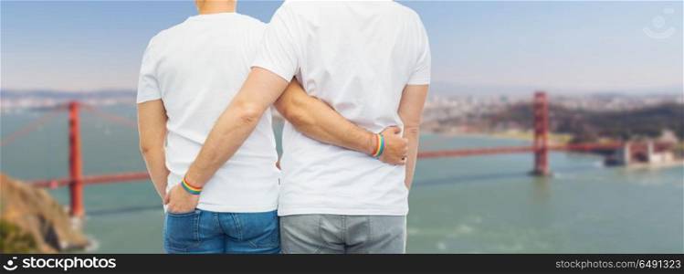 lgbt, same-sex relationships and homosexual concept - close up of hugging male couple wearing rainbow gay pride awareness wristbands over golden gate bridge in san francisco bay background. male couple with gay pride rainbow wristbands. male couple with gay pride rainbow wristbands