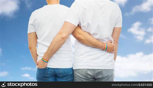 lgbt, same-sex relationships and homosexual concept - close up of hugging male couple wearing rainbow gay pride awareness wristbands over blue sky and clouds background. male couple with gay pride rainbow wristbands. male couple with gay pride rainbow wristbands