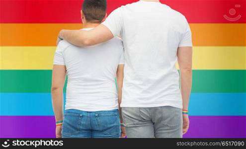 lgbt, same-sex relationships and homosexual concept - close up of hugging male couple wearing gay pride awareness wristbands over rainbow colors background. male couple with gay pride rainbow wristbands. male couple with gay pride rainbow wristbands