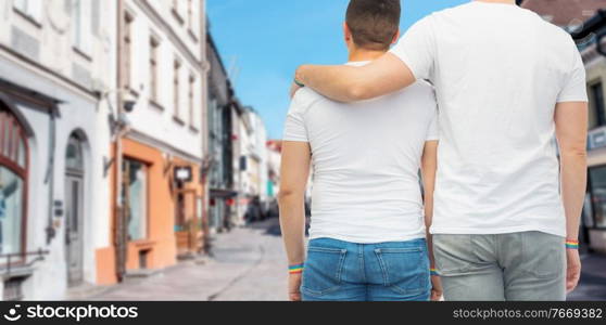 lgbt, same-sex relationships and homosexual concept - close up of hugging male couple wearing gay pride rainbow awareness wristbands over old town street in tallinn city on background. male couple with gay pride wristbands in city