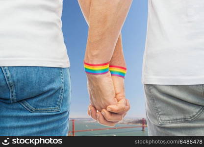 lgbt, same-sex relationships and homosexual concept - close up of male couple wearing gay pride rainbow awareness wristbands holding hands over golden gate bridge in san francisco bay background. male couple with gay pride rainbow wristbands. male couple with gay pride rainbow wristbands