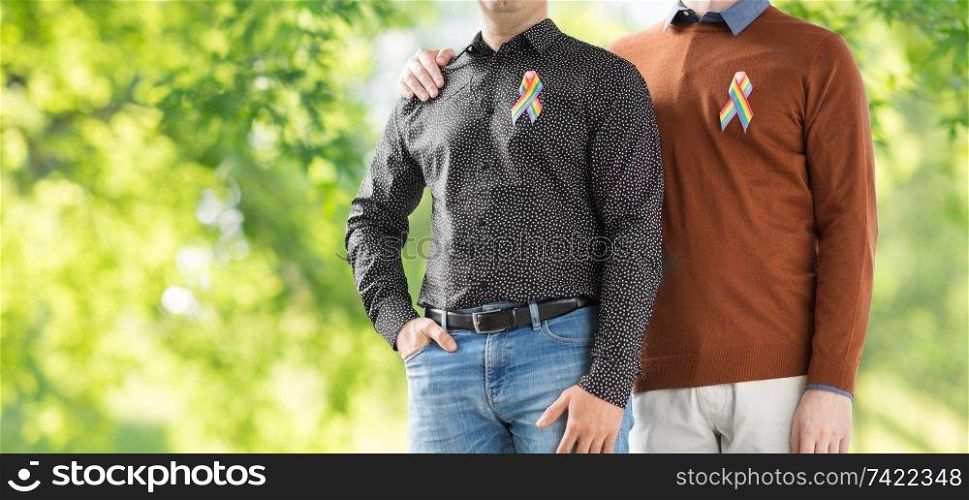 lgbt, same-sex relationships and homosexual concept - close up of male couple with gay pride rainbow awareness ribbons over green natural background. close up of couple with gay pride rainbow ribbons