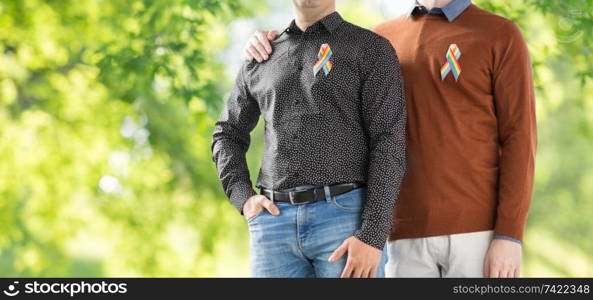lgbt, same-sex relationships and homosexual concept - close up of male couple with gay pride rainbow awareness ribbons over green natural background. close up of couple with gay pride rainbow ribbons