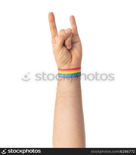lgbt, same-sex relationships and homosexual concept - close up of male hand wearing gay pride awareness wristband showing rock or hand-horns sign. hand with gay pride rainbow wristband shows rock. hand with gay pride rainbow wristband shows rock