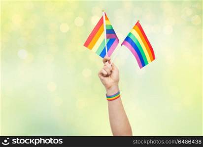 lgbt, same-sex relationships and homosexual concept - close up of male hand wearing gay pride awareness wristband holding rainbow flags over green lights background. hand with gay pride rainbow flags and wristband. hand with gay pride rainbow flags and wristband