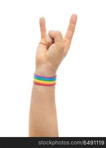 lgbt, same-sex relationships and homosexual concept - close up of male hand wearing gay pride awareness wristband showing rock or hand-horns sign. hand with gay pride rainbow wristband shows rock. hand with gay pride rainbow wristband shows rock