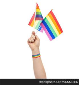 lgbt, same-sex relationships and homosexual concept - close up of male hand wearing gay pride awareness wristband holding rainbow flags. hand with gay pride rainbow flags and wristband. hand with gay pride rainbow flags and wristband