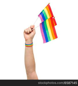 lgbt, same-sex relationships and homosexual concept - close up of male hand wearing gay pride awareness wristband holding rainbow flags. hand with gay pride rainbow flags and wristband