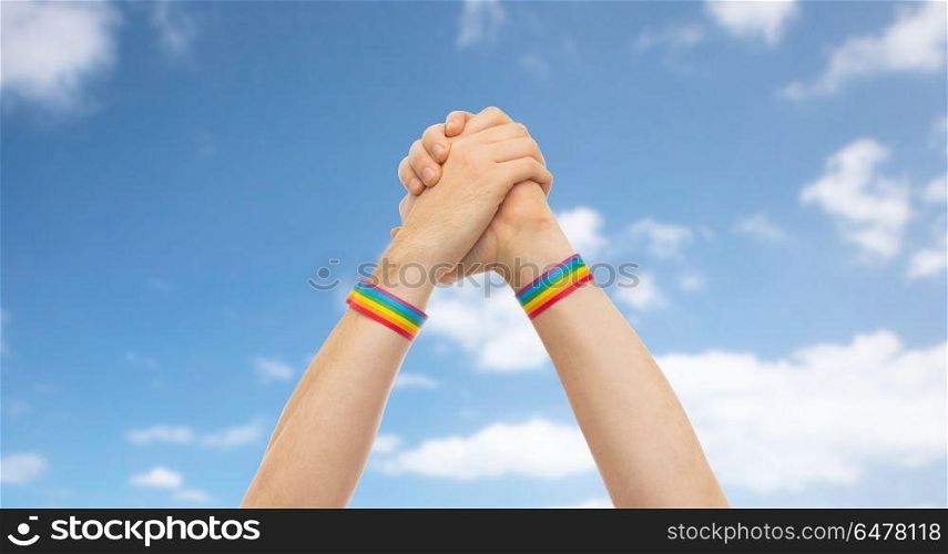 lgbt, same-sex relationships and homosexual concept - close up of male hands wearing gay pride awareness wristbands making winning gesture over blue sky and clouds background. hands with gay pride wristbands in winning gesture. hands with gay pride wristbands in winning gesture