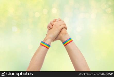 lgbt, same-sex relationships and homosexual concept - close up of male hands wearing gay pride awareness wristbands making winning gesture over green lights background. hands with gay pride wristbands in winning gesture. hands with gay pride wristbands in winning gesture