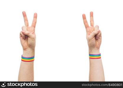 lgbt, same-sex relationships and homosexual concept - close up of male hands wearing gay pride awareness wristbands showing peace sign. hands with gay pride rainbow wristbands make peace. hands with gay pride rainbow wristbands make peace
