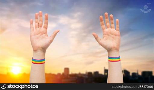lgbt, same-sex relationships and homosexual concept - close up of male hands wearing gay pride awareness wristbands over city sunset background. hands with gay pride rainbow wristbands. hands with gay pride rainbow wristbands