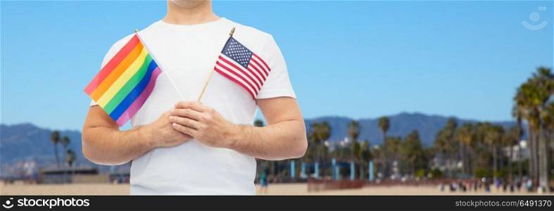 lgbt, same-sex relationships and homosexual concept - close up of man holding gay pride rainbow and american flag over venice beach background in california. man with gay pride rainbow flag and american. man with gay pride rainbow flag and american