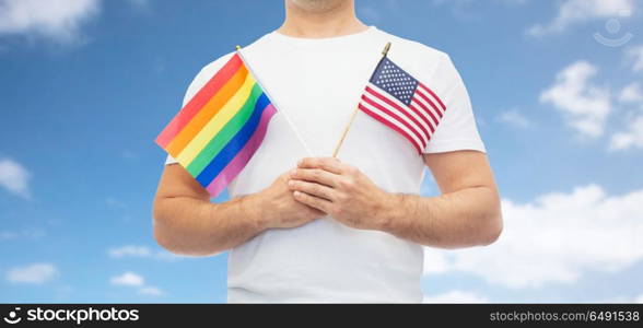 lgbt, same-sex relationships and homosexual concept - close up of man holding gay pride rainbow and american flag over blue sky and clouds background. man with gay pride rainbow flag and american. man with gay pride rainbow flag and american