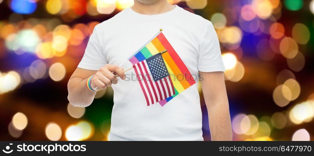 lgbt, same-sex relationships and homosexual concept - close up of man wearing gay pride rainbow awareness wristband and holding american flag over lights background. man with gay pride rainbow flag and wristband. man with gay pride rainbow flag and wristband