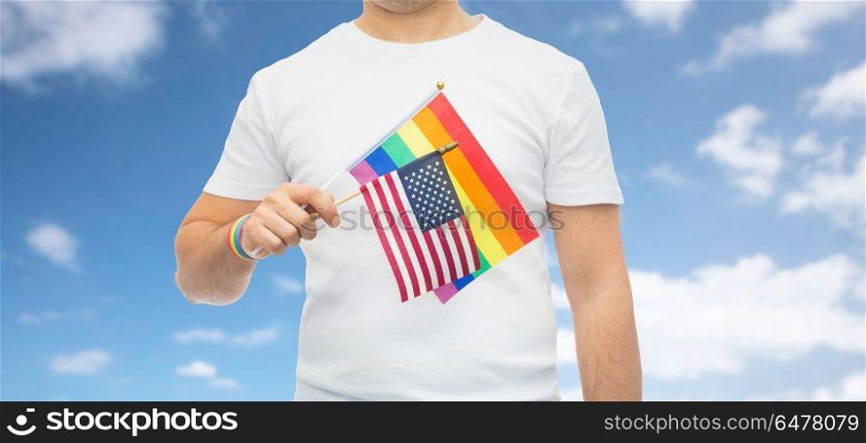 lgbt, same-sex relationships and homosexual concept - close up of man wearing gay pride rainbow awareness wristband and holding american flag over blue sky and clouds background. man with gay pride rainbow flag and wristband. man with gay pride rainbow flag and wristband