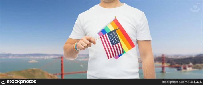 lgbt, same-sex relationships and homosexual concept - close up of man wearing gay pride rainbow awareness wristband and holding american flag over golden gate bridge in san francisco bay background. man with gay pride rainbow flag and wristband. man with gay pride rainbow flag and wristband