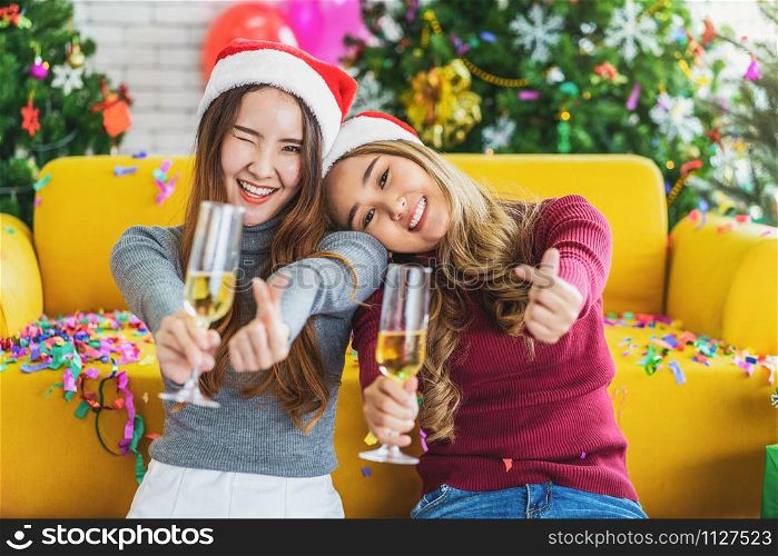 LGBTQ couple asian happiness women wearing colorful red sweaters holding and cheering with doing mini hearth action in christmas party with xmas trees, asian or asean indoor, xmas and new year concept