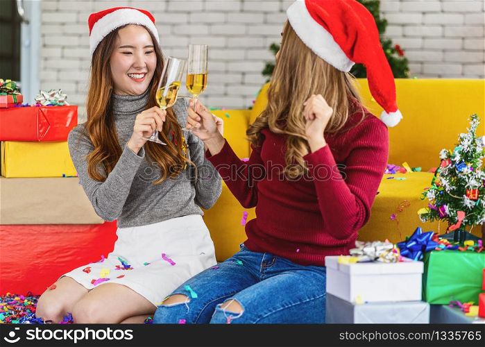LGBTQ couple asian happiness women wearing colorful red sweaters holding and cheering prosecco in christmas party with xmas trees, asian or asean indoor house, xmas and new year concept