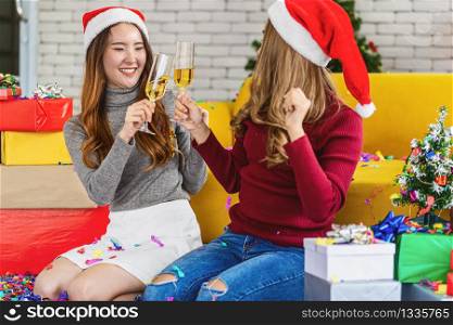 LGBTQ couple asian happiness women wearing colorful red sweaters holding and cheering prosecco in christmas party with xmas trees, asian or asean indoor house, xmas and new year concept