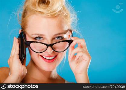 Librarian, accountant and secretary concept. Retro, pin up style. Young blonde woman in glasses. Girl holding smartphone on blue background in studio.