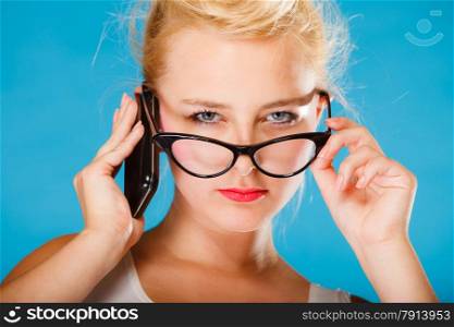 Librarian, accountant and secretary concept. Retro, pin up style. Young blonde woman looking through glasses. Girl holding smartphone on blue background in studio.