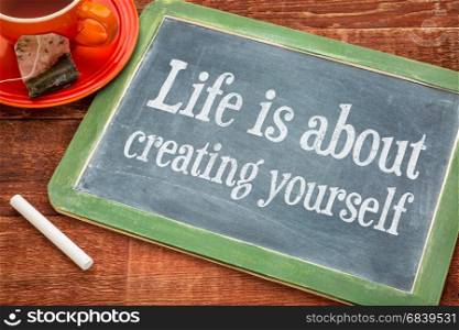 Life is about creating yourself - motivational text on a slate blackboard with chalk and cup of tea